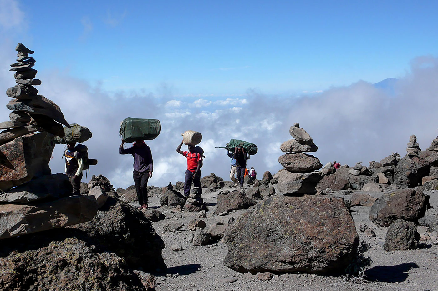 Porters carrying equipment across rocky desert with stone cairns on Mount Kilimanjaro – Tanzania trekking expedition  with Pizet Safaris